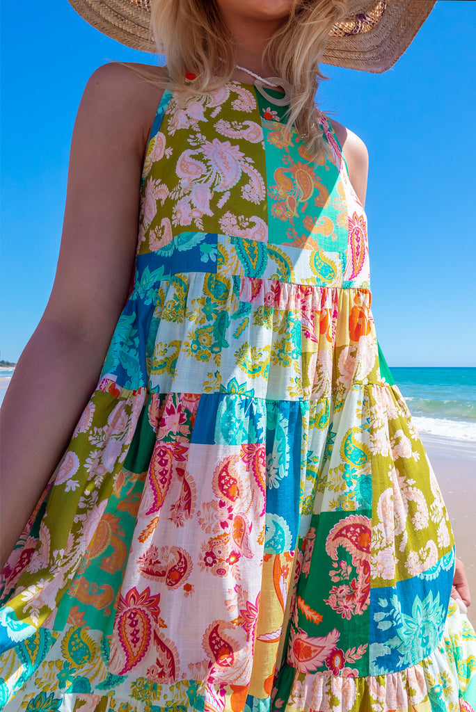 The Lulu Darling Green Glow Maxi Dress features a high neck with thin straps, high cut under arms, full tiered skirting from the bust down and deep side pockets. The dress has a green patchwork print with multicoloured paisley designs. Made from 100% cotton.