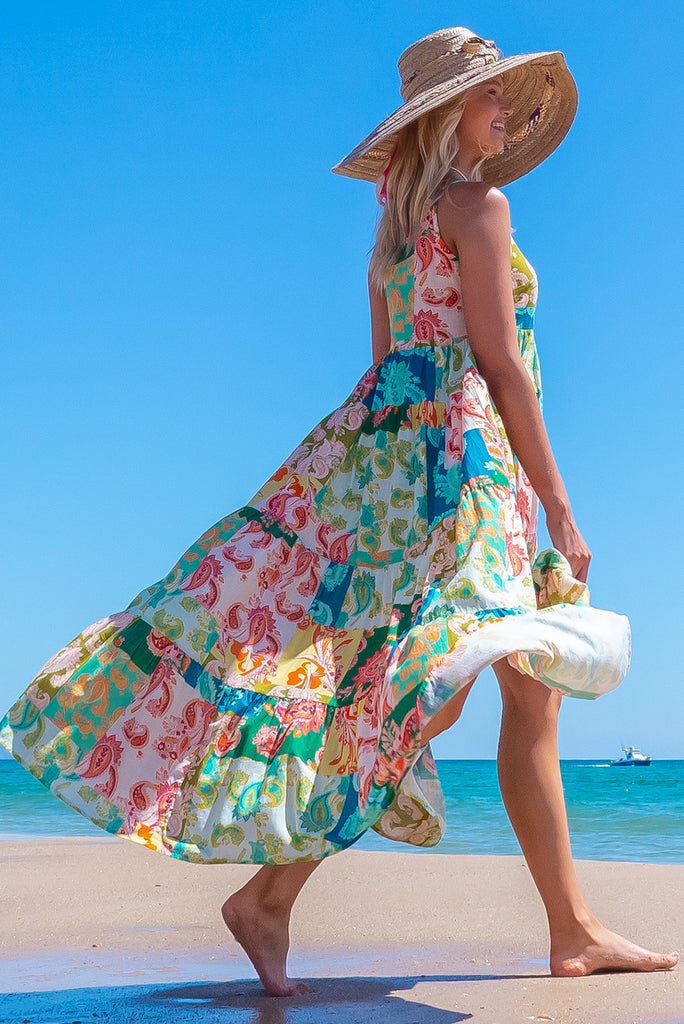 The Lulu Darling Green Glow Maxi Dress features a high neck with thin straps, high cut under arms, full tiered skirting from the bust down and deep side pockets. The dress has a green patchwork print with multicoloured paisley designs. Made from 100% cotton.