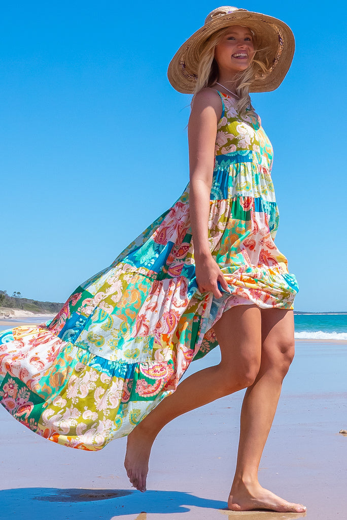 The Lulu Darling Green Glow Maxi Dress features a high neck with thin straps, high cut under arms, full tiered skirting from the bust down and deep side pockets. The dress has a green patchwork print with multicoloured paisley designs. Made from 100% cotton.