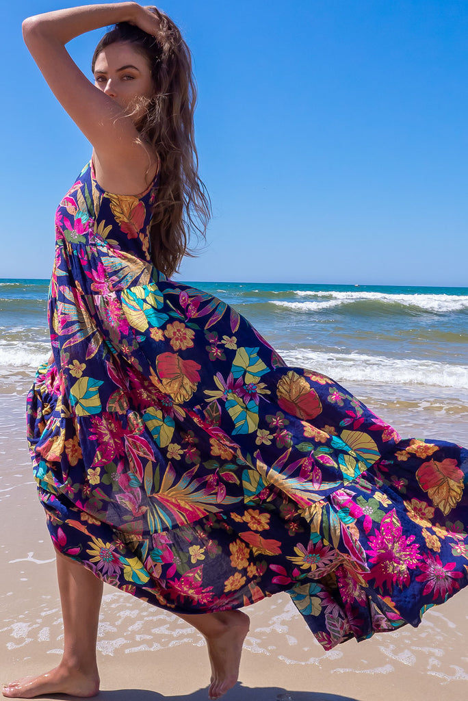 The Lulu Darling Paradise Navy Maxi Dress is a striking dress with an ink navy base and large tropical print. The maxi dress features a high neck, high cut under the arms, full tiered skirt falling from under bust, side pockets, and is woven cotton/rayon blend.