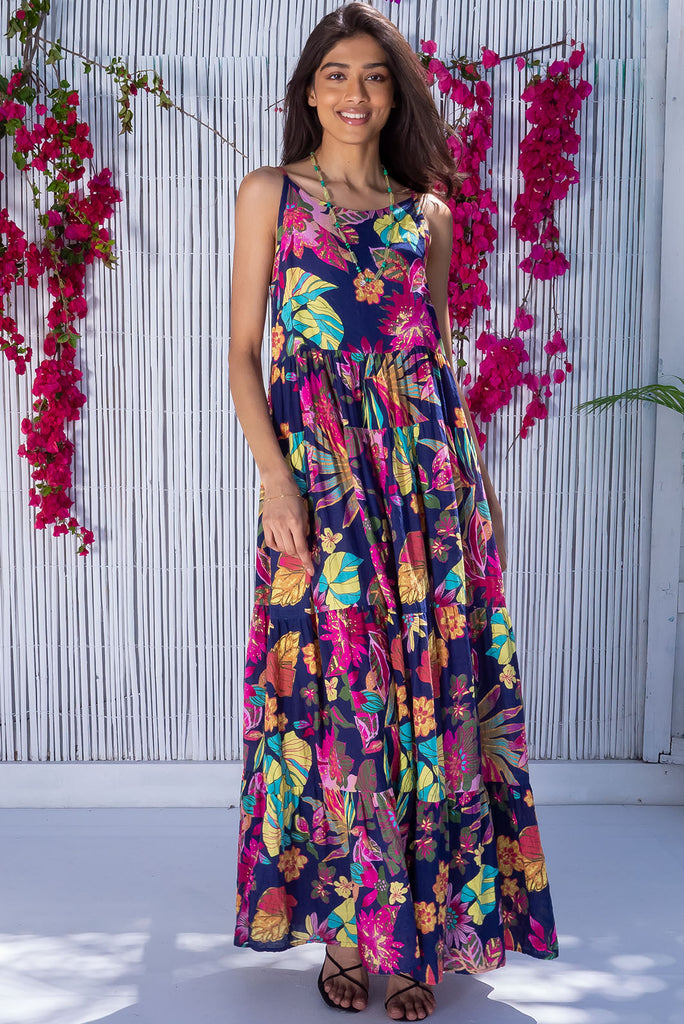 The Lulu Darling Paradise Navy Maxi Dress is a striking dress with an ink navy base and large tropical print. The maxi dress features a high neck, high cut under the arms, full tiered skirt falling from under bust, side pockets, and is woven cotton/rayon blend.