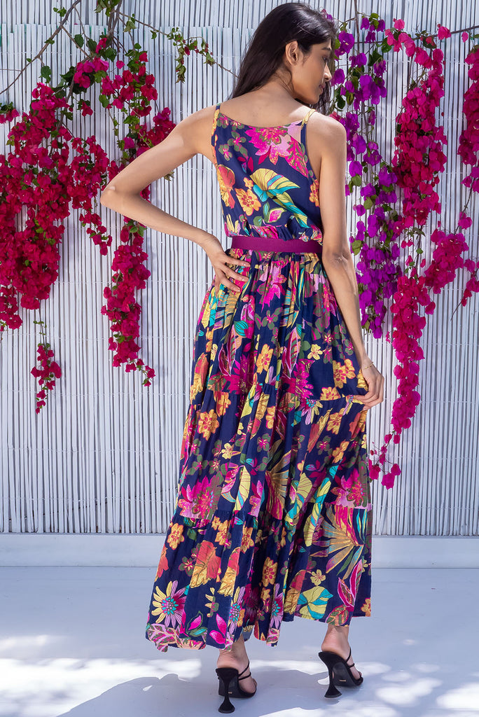 The Lulu Darling Paradise Navy Maxi Dress is a striking dress with an ink navy base and large tropical print. The maxi dress features a high neck, high cut under the arms, full tiered skirt falling from under bust, side pockets, and is woven cotton/rayon blend.