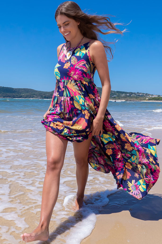 The Lulu Darling Paradise Navy Maxi Dress is a striking dress with an ink navy base and large tropical print. The maxi dress features a high neck, high cut under the arms, full tiered skirt falling from under bust, side pockets, and is woven cotton/rayon blend.