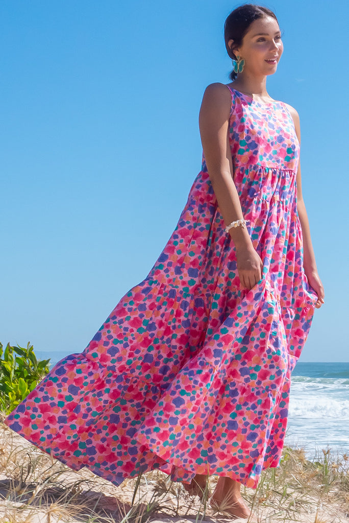 The Lulu Darling Sea Shells Pink Tiered Maxi Dress features a high neck with thin straps, high cut under arms, full tiered skirting from the bust down and deep side pockets. The pink based dress has a multicoloured seashell print all over in. Made from 100% cotton poplin.