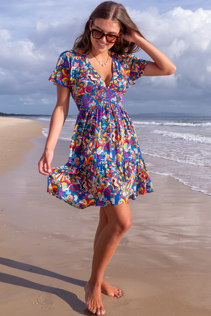 The Mirabella 60s Print Dress is a bold deep blue based mini dress with a vibrant multicoloured pop art retro print. The mini dress features a lined bust, v neckline, drop flutter sleeves, low v back with tie at the top, cinched elastic waist, tiered skirt and side pockets. This dress is made from woven 100% rayon.