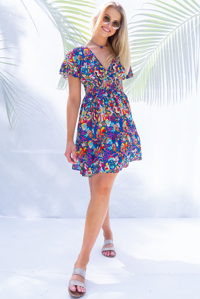 The Mirabella 60s Print Dress is a bold deep blue based mini dress with a vibrant multicoloured pop art retro print. The mini dress features a lined bust, v neckline, drop flutter sleeves, low v back with tie at the top, cinched elastic waist, tiered skirt and side pockets. This dress is made from woven 100% rayon.