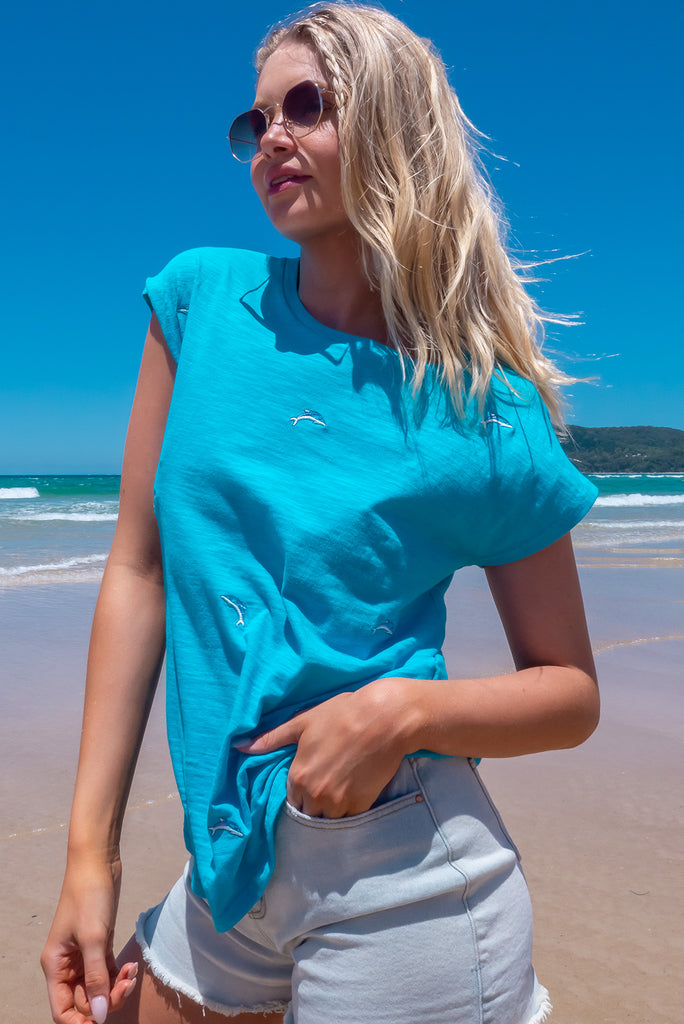 The Paradise Blue Dolphin Embroidered T-Shirt is a sky blue t-shirt with embroidered dolphins all over. This shirt has a soft, classic t-shirt cut, and curved hem. Made from knit 100% cotton.