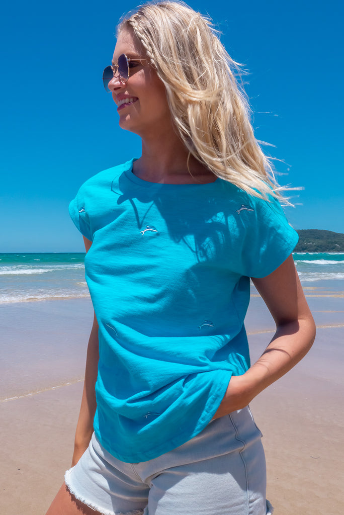 The Paradise Blue Dolphin Embroidered T-Shirt is a sky blue t-shirt with embroidered dolphins all over. This shirt has a soft, classic t-shirt cut, and curved hem. Made from knit 100% cotton.