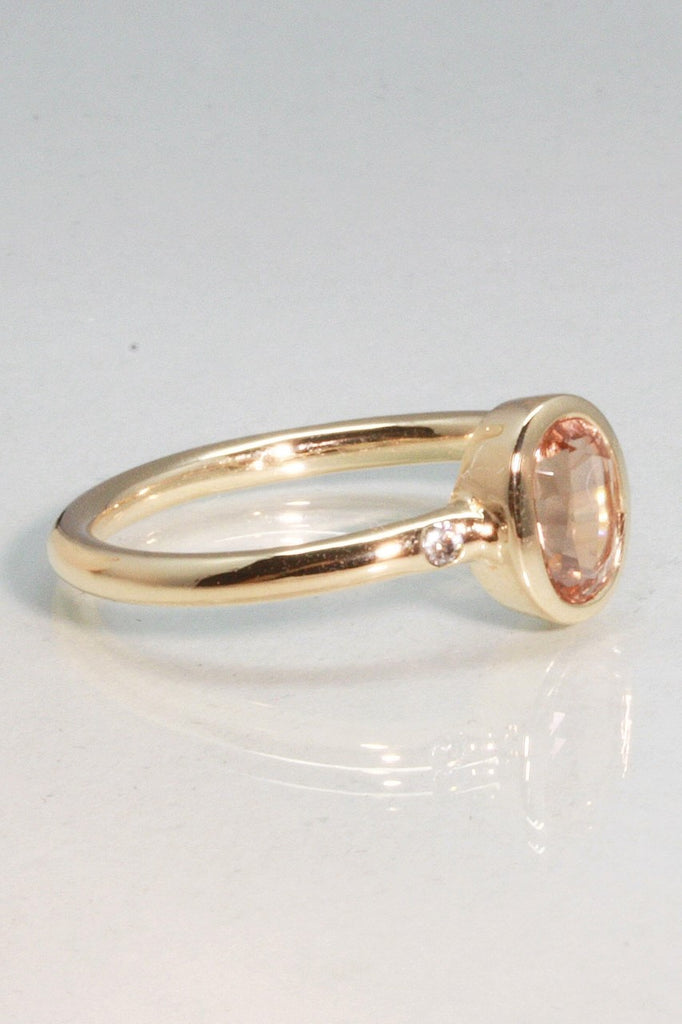 A beautiful simple ring designed to complement the lovely natural pale peach pink tourmaline gemstone set into the ring. The shank of the ring has a diamond on each side of the centre stone. 