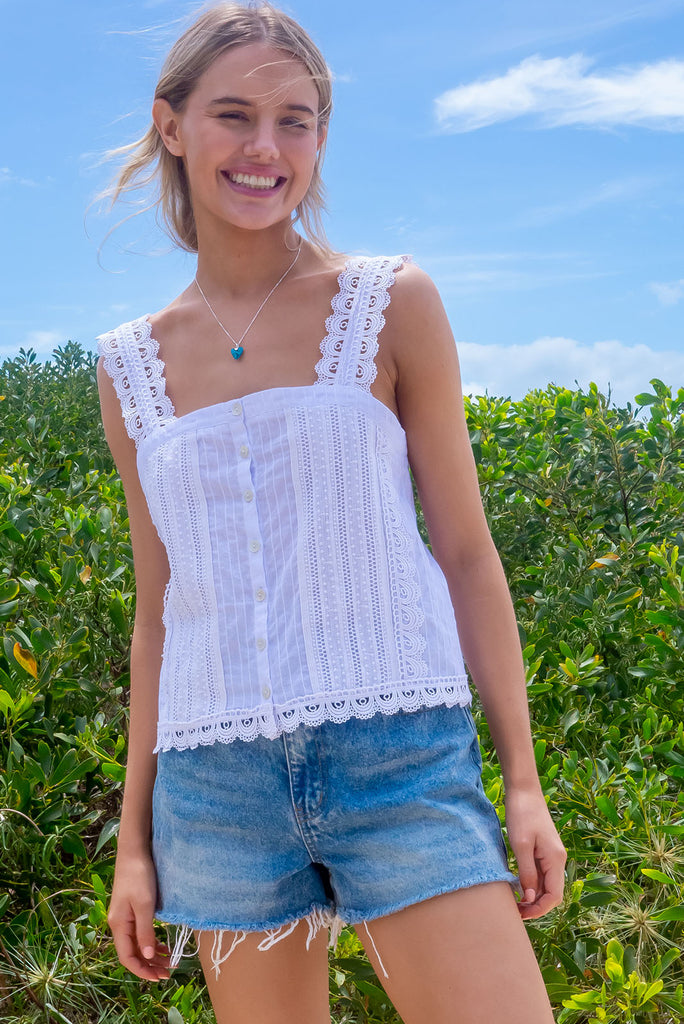 The Positano White Lace Cami Top is a beautiful white coloured textured cami top with lace detailing on the straps, front and hem. The shirt also features a functional shell button front.