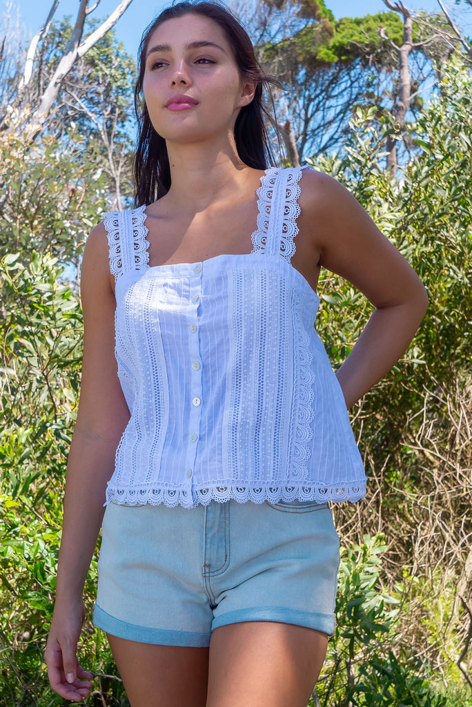 The Positano White Lace Cami Top is a beautiful white coloured textured cami top with lace detailing on the straps, front and hem. The shirt also features a functional shell button front.