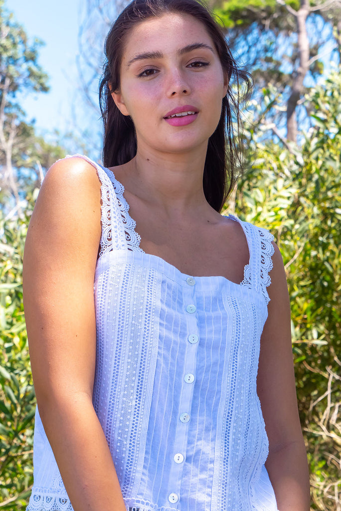 The Positano White Lace Cami Top is a beautiful white coloured textured cami top with lace detailing on the straps, front and hem. The shirt also features a functional shell button front.