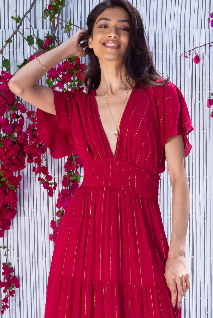 The Romance Dark Red Maxi Dress is a stunning rich red tone maxi dress with textured spots and lurex stripes. The dress features a lined bust, deep plunge v neckline, drop flutter sleeves, low v back with tie at the top, cinched elastic was it, full tiered skirt and side pockets. This dress is made from woven 100% crinkle viscose. 