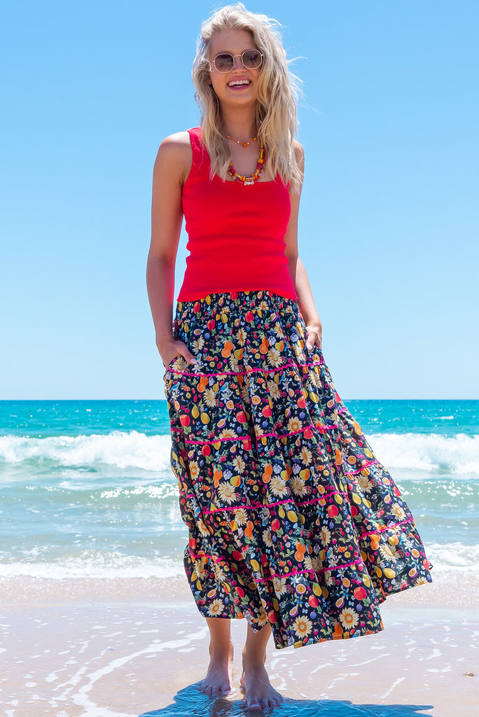 The Rozita Summer Fruit Tiered Maxi Skirt is a stunning black based maxi skirt with a summer fruit and flower print all over. The maxi skirt features side pockets, tiering, red ric-rac on each tier and an elasticated waistband. Made from 100% cotton.