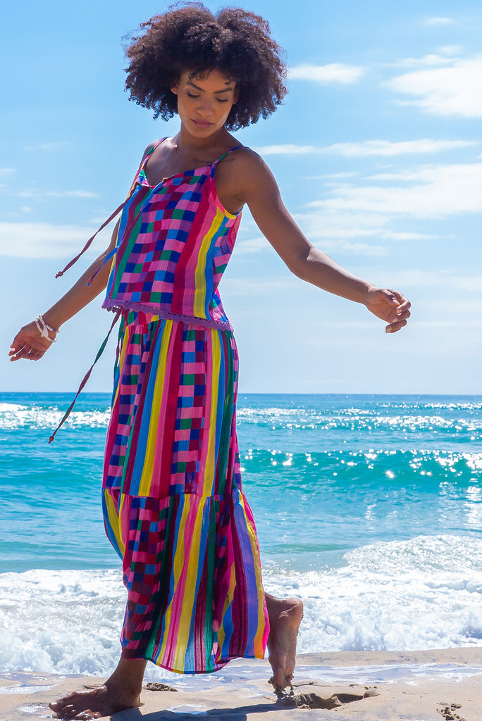 The Valencia Carnivale Maxi Skirt is a vibrant and fun skirt featuring elasticated waistband with decorative tie, side pockets and Woven fabric 95% cotton 5% polyester in vibrant multi coloured check and stripe print with a lurex thread running through.