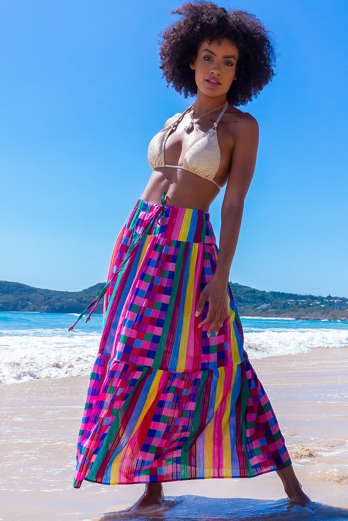 The Valencia Carnivale Maxi Skirt is a vibrant and fun skirt featuring elasticated waistband with decorative tie, side pockets and Woven fabric 95% cotton 5% polyester in vibrant multi coloured check and stripe print with a lurex thread running through.
