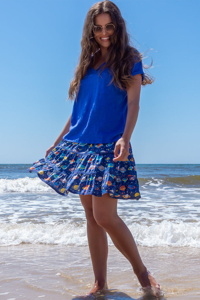 The Ziggy Cosmic Blue Mini Skirt is a retro-chic medium blue mini skirt with a planet print. The skirt features a shirred waistband, comfortable pull-on style, tiered, lace detailing and side pockets. This mini skirt is made from woven 100% cotton.