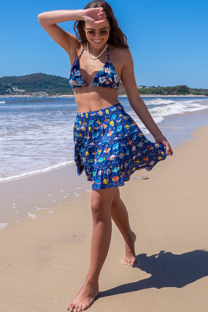The Ziggy Cosmic Blue Mini Skirt is a retro-chic medium blue mini skirt with a planet print. The skirt features a shirred waistband, comfortable pull-on style, tiered, lace detailing and side pockets. This mini skirt is made from woven 100% cotton.