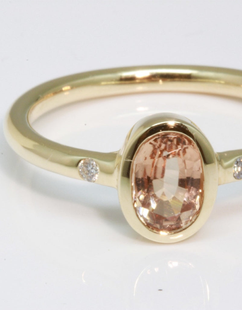 A beautiful simple ring designed to complement the lovely natural pale peach pink tourmaline gemstone set into the ring. The shank of the ring has a diamond on each side of the centre stone. 